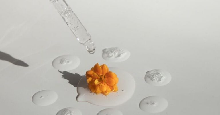 Minimal Viable Product - From above of drops of transparent moisturizing cosmetic product dripped by pipette and small fresh flower head placed on white table